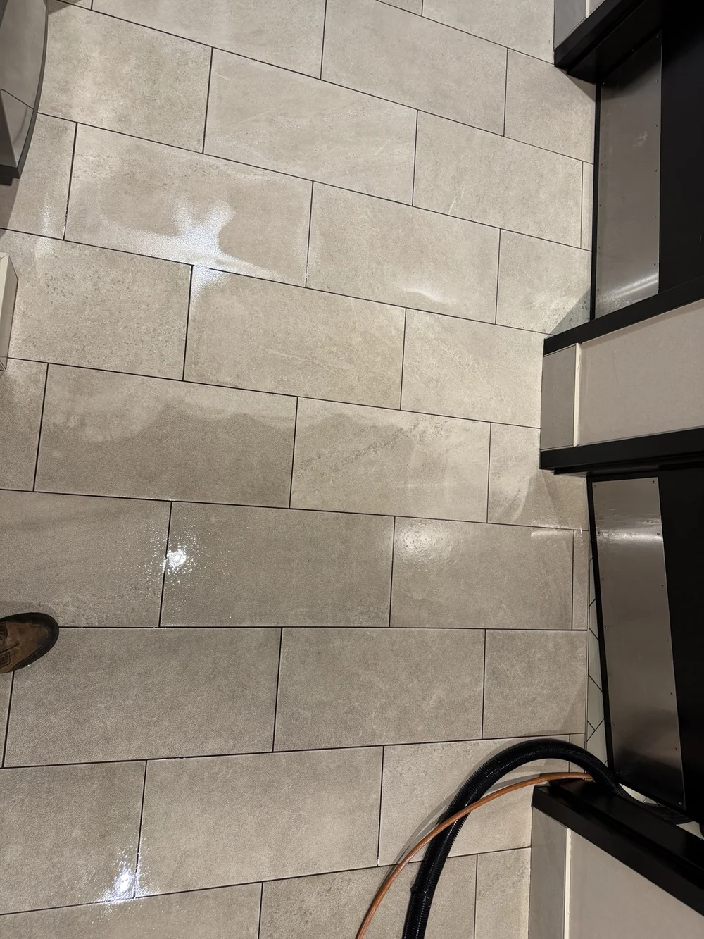 Large-format tile floor during cleaning, with wet areas and hoses